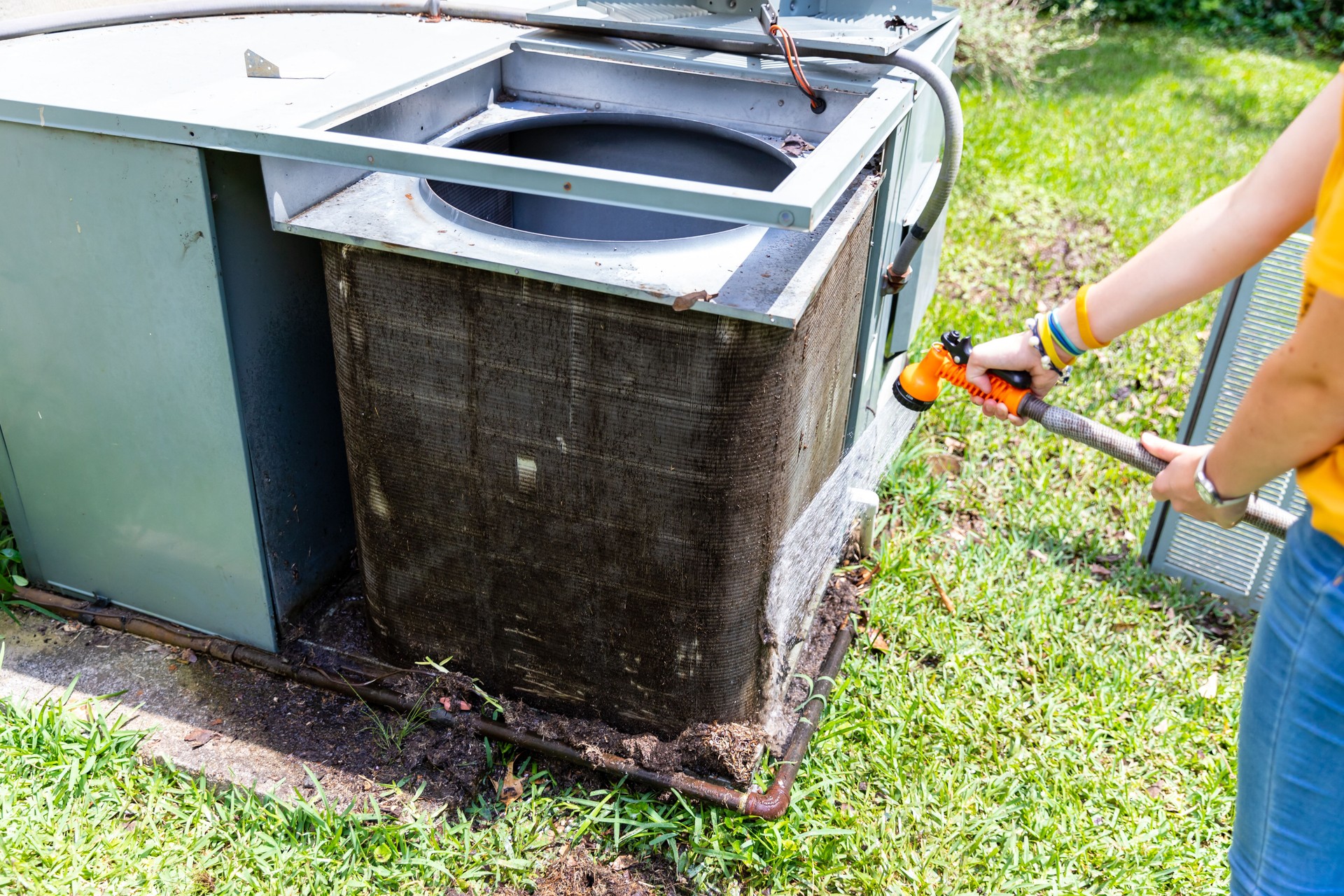 Person cleaning dirty condenser coils on an air conditioner system